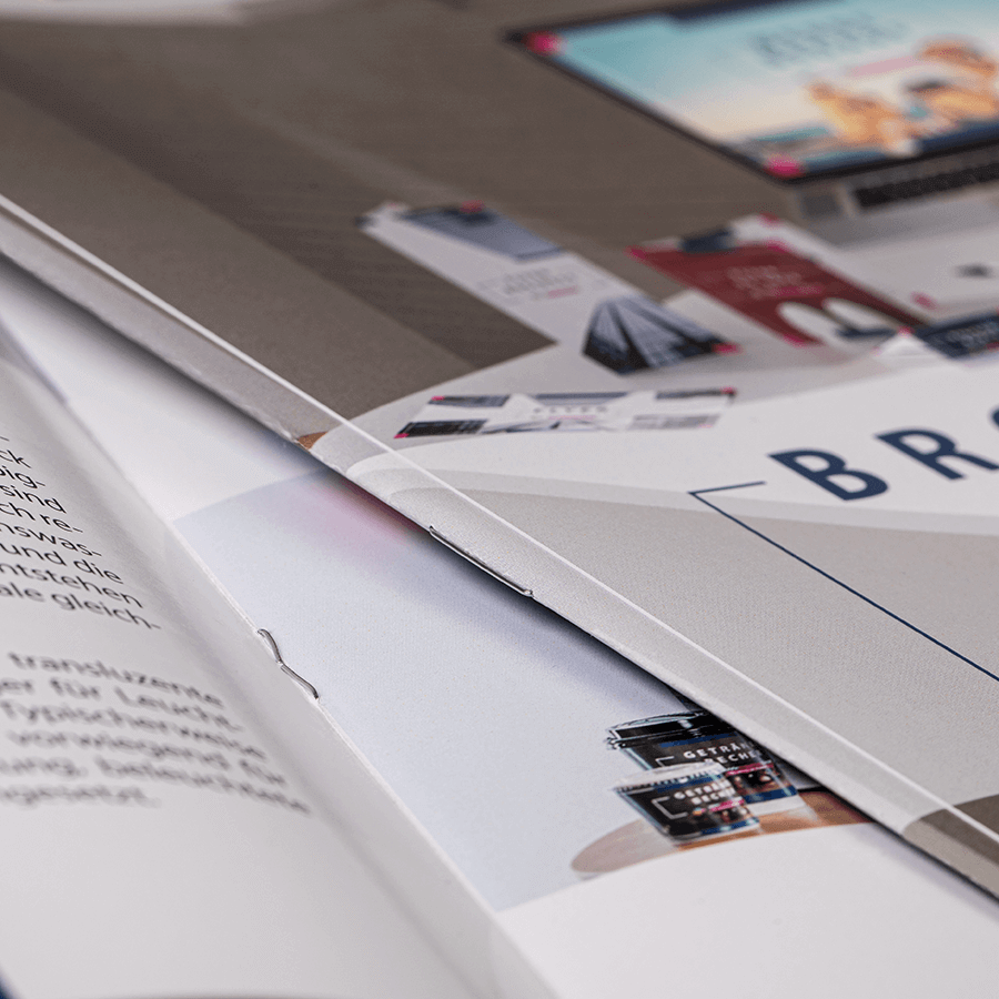 Zwei Broschüren mit Drahtheftung, aufgeschlagen und zugeklappt, mit Drahtheftung in Detailansicht