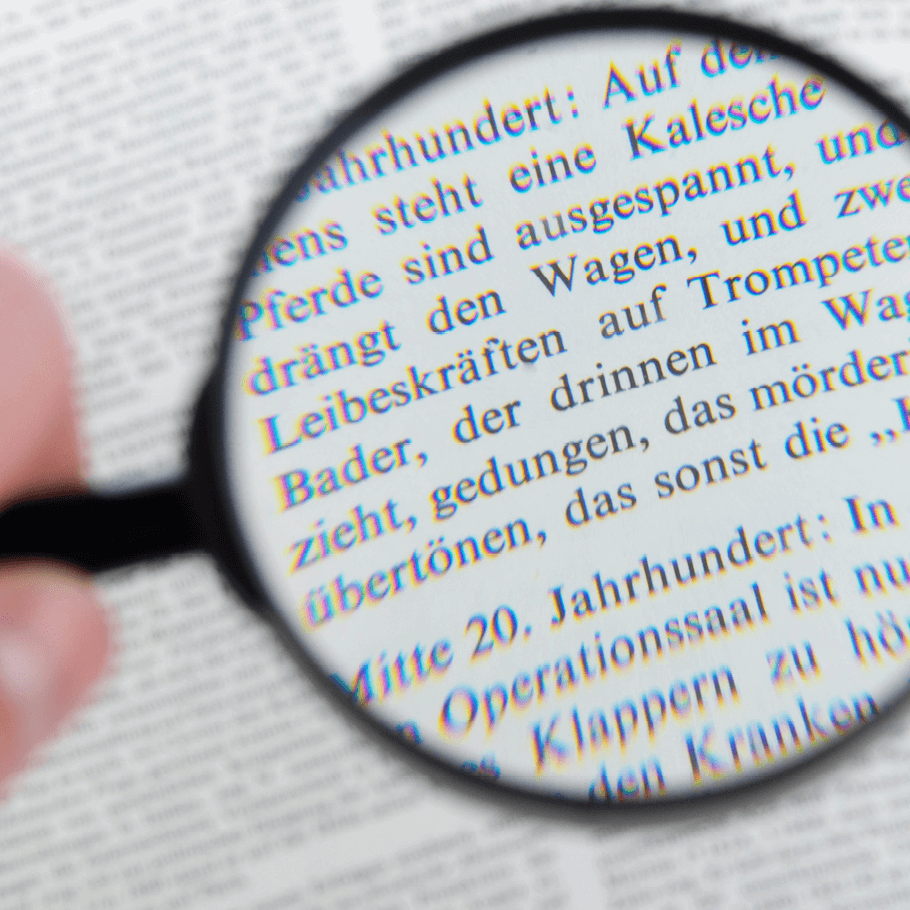 Hand mit schwarzer Lupe über längerer Textpassage in kleiner Schriftgröße