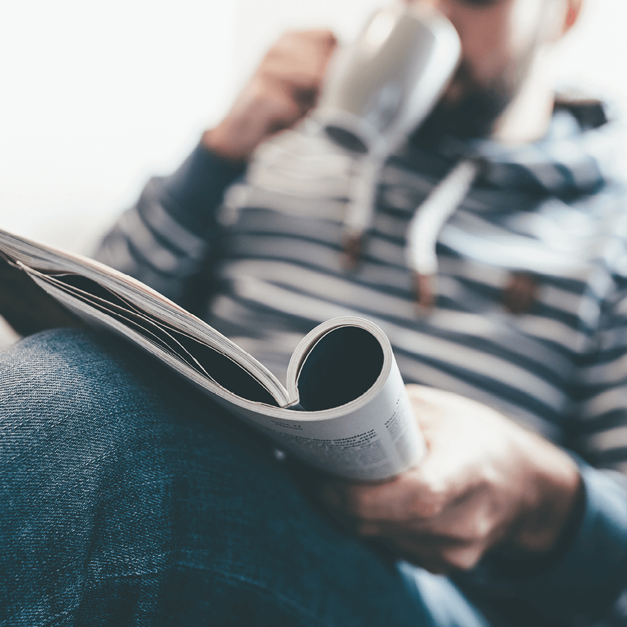 Mann liest in Magazin mit typischer Schriftgröße und trinkt aus Kaffeetasse.