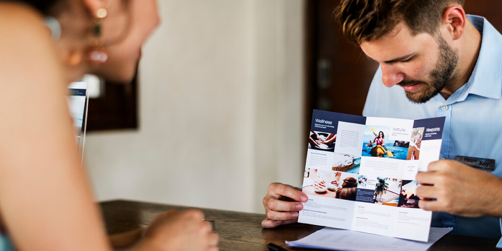 Flyer mit Wickelfalz, eine der aufklappbaren Falzarten, in den Händen eines Rezeptionisten