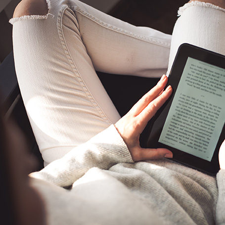Selfpublishing von E-Books: von oben aufgenommene Person mit E-Reader auf dem Oberschenkel