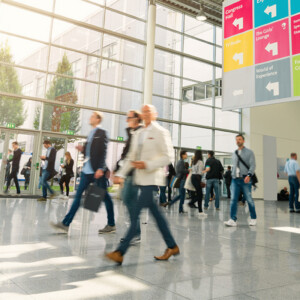 Mehrere Menschen durchqueren eine Messehalle und erwarten einen erfolgreichen Messeauftritt.