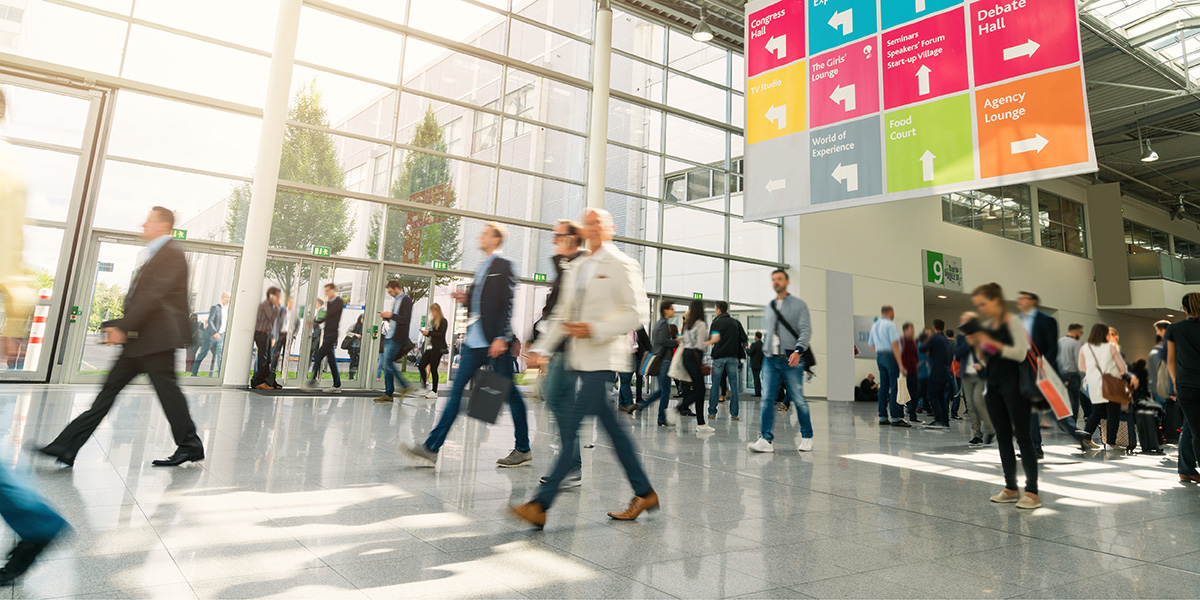 Mehrere Menschen durchqueren eine Messehalle und erwarten einen erfolgreichen Messeauftritt.
