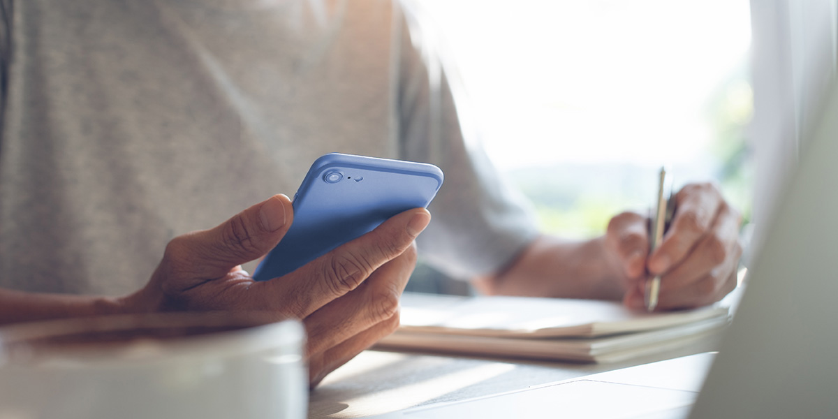 Marketing fürs Selfpublishing: Person vor Laptop mit Handy und Stift in den Händen