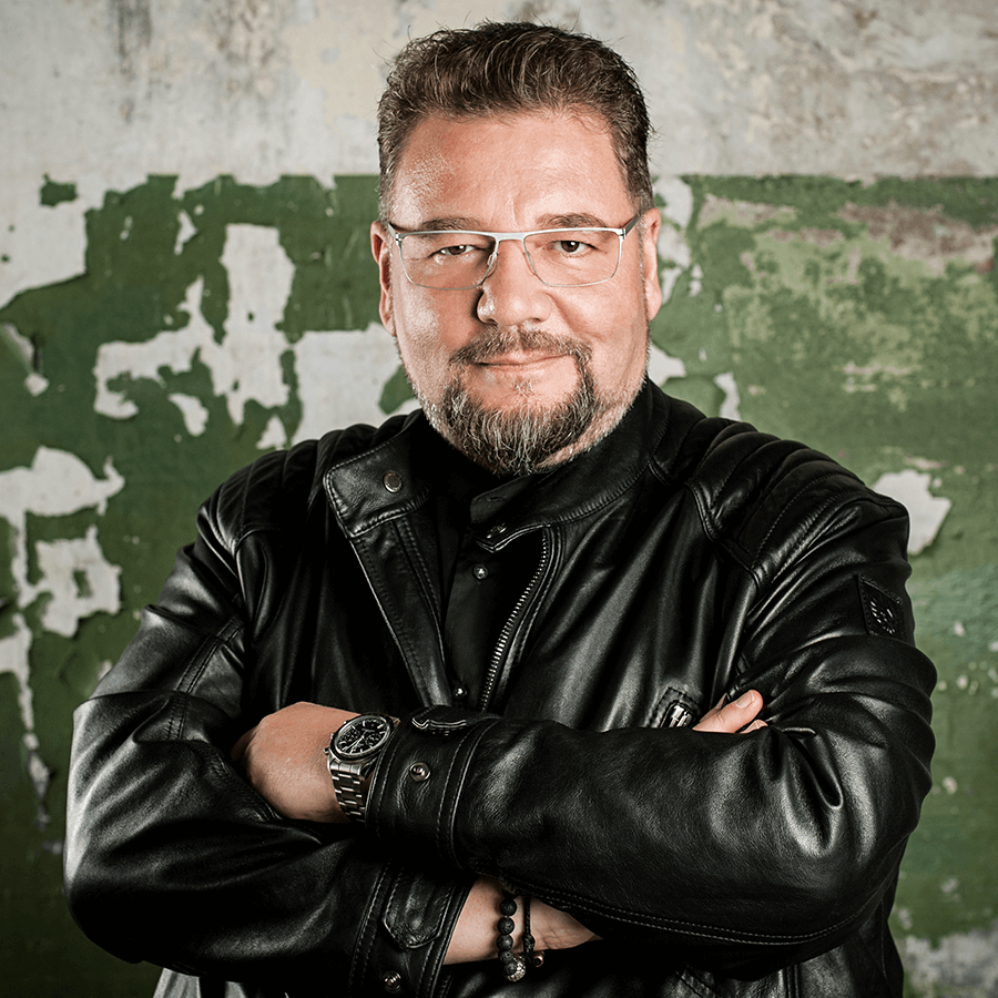 Druckexperte Bernd Zipper mit verschränkten Armen & Onlineliebe in schwarzer Lederjacke vor Wand