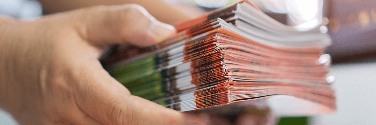 Onlinedruckliebe: eine Person hält einen Stapel gedruckter, bunter Broschüren in den Händen