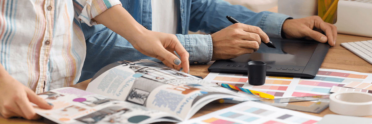 Onlinedruckliebe: 2 Personen beim Designen von Druckprodukten mit Broschüre, Farbkarten und Tablet