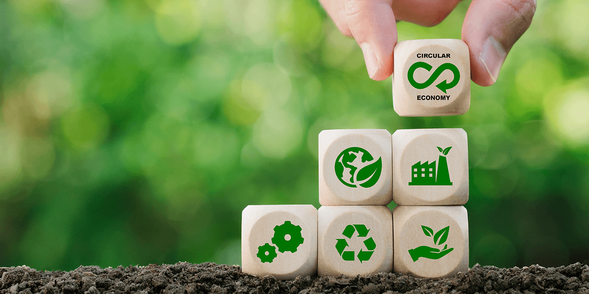 Eine Person legt Bauklötze mit grünen Icons zur nachhaltigen Kreislaufwirtschaft aufeinander