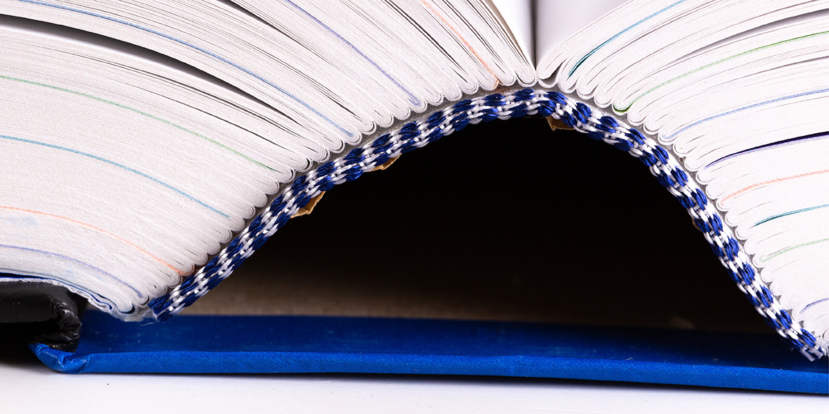 Bindeart Fadenheftung: Nahaufnahme der Bindung eines aufgeschlagenen blauen Hardcover-Buchs