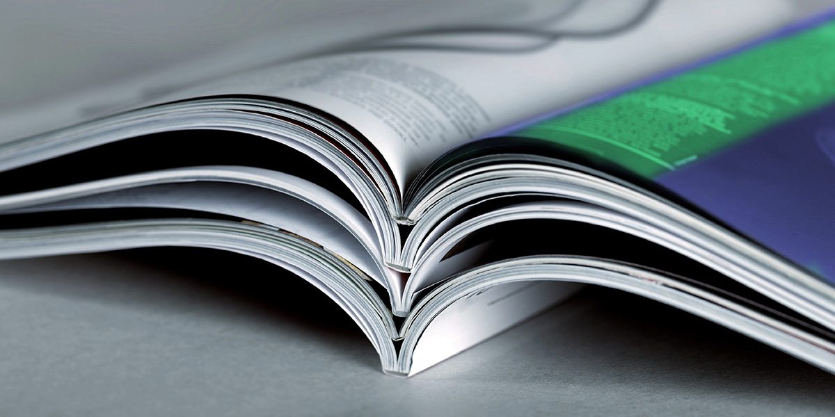 Die Bindeart Klebebindung: Nahaufnahme von 5 Magazinen, die aufgeschlagen und übereinandergelegt sind