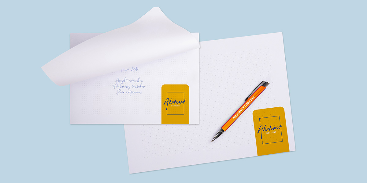 Zwei Blöcke mit der Bindeart Leimung auf hellblauem Hintergrund mit Stift, alles mit Branding