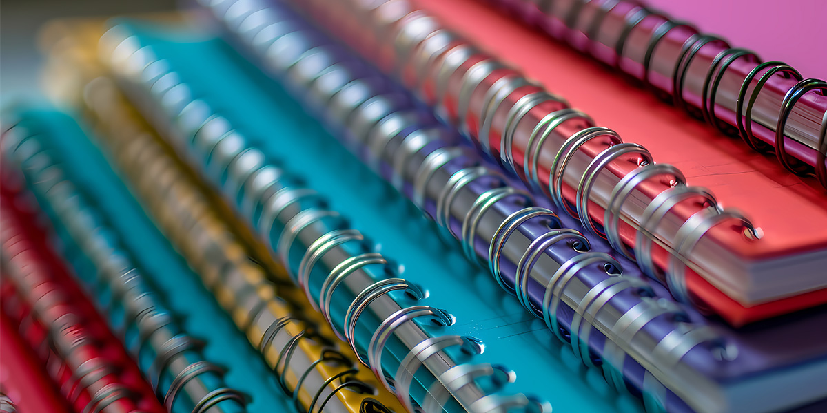 Die Bindeart Spiralbindung: Nahaufnahme von vielen gestapelten Notizbüchern in verschiedenen Farben