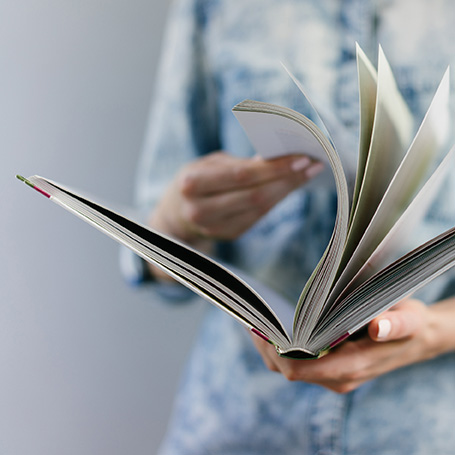 Eine Person in einem hellblauen-weißen Hemd blättert in einem Hardcover-Buch