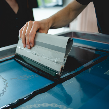 Person beim Siebdruck (T-Shirt-Druckverfahren): verteilt Farbe mit Rakel