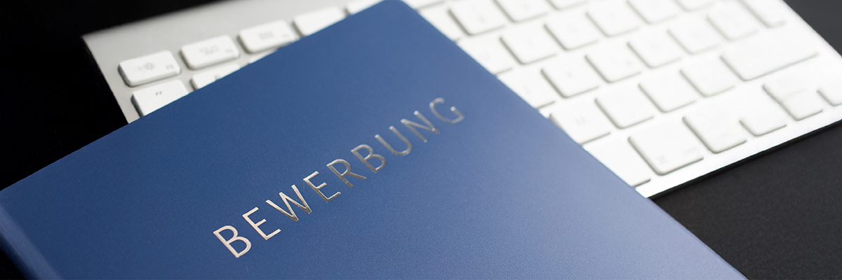 Eine blaue Bewerbungsmappe mit glänzender Aufschrift liegt auf einer weißen Tastatur