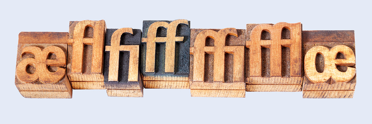 Sieben Drucktypen aus Holz mit Ligaturen auf hellblauem Hintergrund