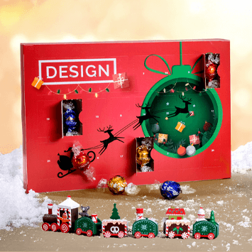 Roter Adventskalender mit Lindt-Kugeln, bedruckt mit Design, davor Schnee und Spielzeugeisenbahn