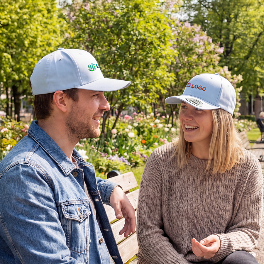 Ein Mann und eine Frau mit personalisierten FLEXFIT-Caps sitzen auf einer Parkbank