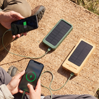 Zwei Solar-Powerbanks in der Sonne liegend, die jeweils ein Handy per Kabel aufladen