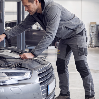 Ein Mann in bestickter Premium-Arbeitshose arbeitet an einem Auto