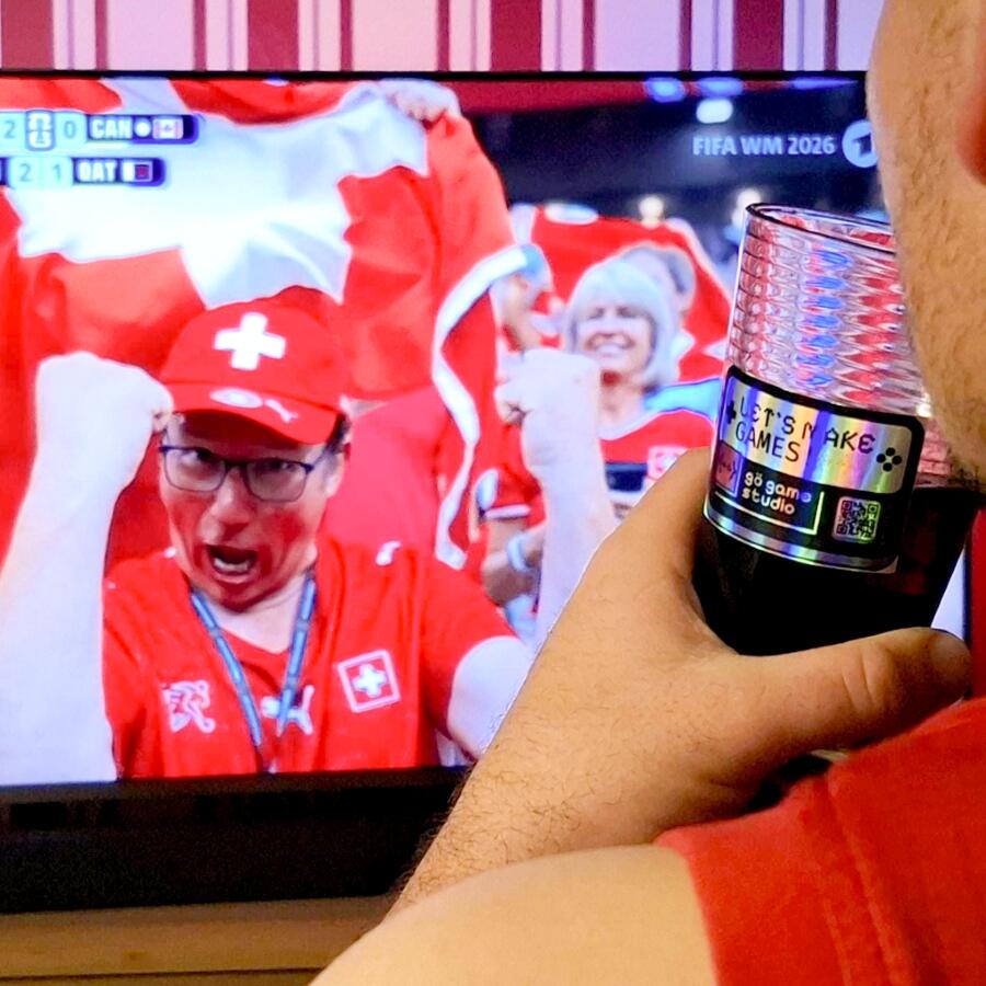 Einsendung WIRmachenFANS-Gewinnspiel: Glas mit bedrucktem Holosticker vor TV mit WM-Spiel