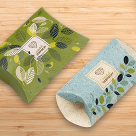 Zwei mit eigenem Design bedruckte Kissenverpackungen in Grün und Hellblau auf einem Holztisch